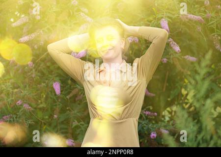 Femme émotive s'amusant à l'extérieur près des fleurs de la Buddleia. Portrait d'une belle blonde sur le coucher de soleil dans la nature. Banque D'Images