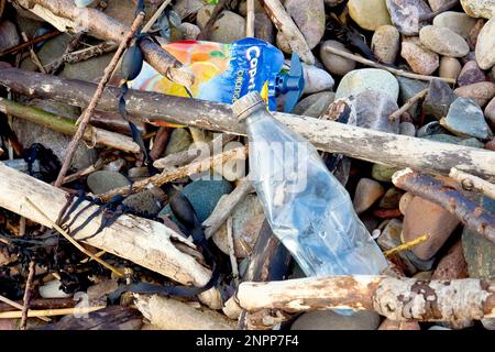 Gros plan des contenants en plastique à usage unique jetés lavés sur une plage de galets. Banque D'Images