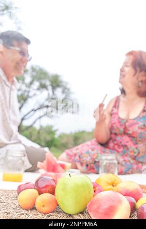 Couple senior ayant un petit déjeuner pique-nique avec une variété de fruits frais, pommes, pêches, mandarines, prunes, pastèque. Concentrez-vous sur eux. Concepts: Healt Banque D'Images