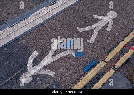 Figures piétonnes peintes sur la route à côté de lignes jaunes doubles le 7th février 2023 à Londres, Royaume-Uni. Banque D'Images