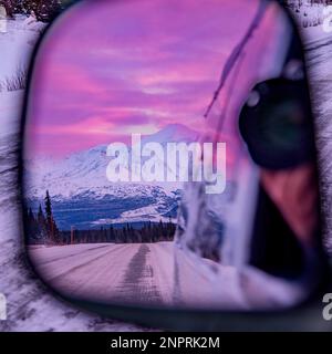 Coucher de soleil rose à partir d'une voiture en hiver avec photo prise dans le rétroviseur du véhicule. Banque D'Images