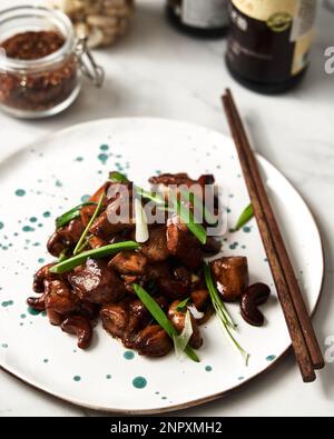 Plat de poulet à la noix de cajou thaï sur la table avec des oignons verts et des bâtonnets de bois. Arrière-plan blanc, Banque D'Images