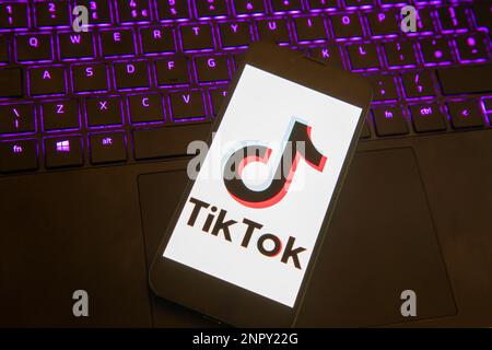 IPhone avec application Tik Tok se chargeant sur un ordinateur portable éclairé Banque D'Images