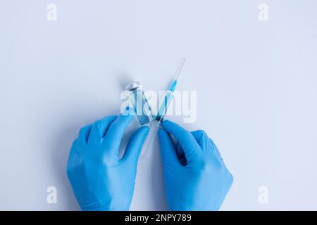 Sur fond blanc isolé, les mains du médecin en gants médicaux bleus tiennent une ampoule avec une seringue en forme de V - Victory. Vaccin contre le vir Banque D'Images