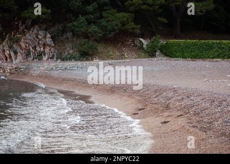 Plage royale avec de petits galets au Monténégro. La marée de la mer sur le rivage. Forêt verte de pins sur le fond. Belle nature. Déplacement Banque D'Images