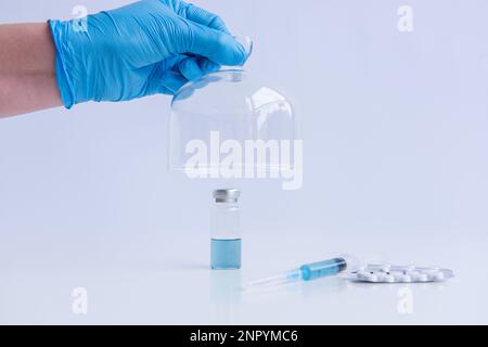 Sur fond blanc isolé se trouve le vaccin avec seringue, pilules. Le gant médical bleu ouvre le dôme de protection programmé. Contre-traiter Banque D'Images
