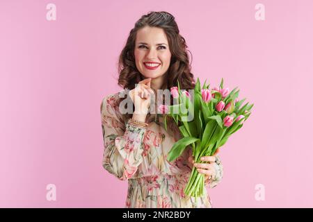 pensive élégante femme d'âge moyen avec de longs cheveux ondulés de brunette avec bouquet de tulipes isolé sur rose. Banque D'Images