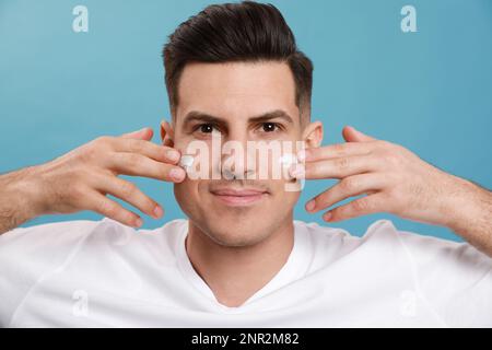 Beau homme appliquant de la crème pour le visage sur fond turquoise Banque D'Images