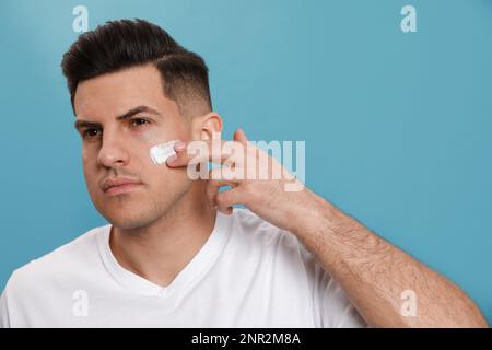 Beau homme appliquant de la crème pour le visage sur fond turquoise Banque D'Images