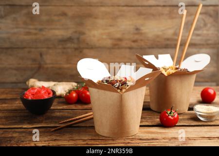 Boîtes de nouilles wok avec fruits de mer et baguettes sur table en bois Banque D'Images