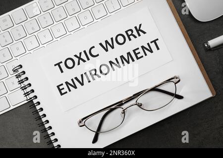 Carnet avec texte Toxic Work Environment sur table noire, plat Banque D'Images