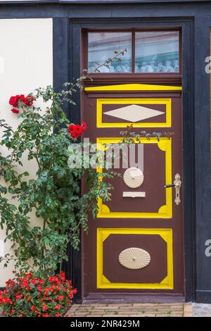 Façade de maison à colombages avec garniture marron et jaune, porte d'entrée en bois peinte et rosier rouge, fleurs Begonia rouges à la fin de l'été. Banque D'Images