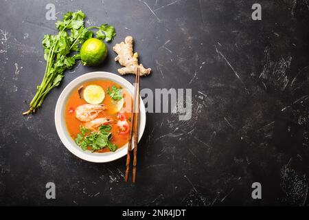 Soupe thaïlandaise traditionnelle épicée et chaude tom yum avec crevettes, citron vert, coriandre dans un bol sur fond de pierre rustique avec espace pour le texte, vue du dessus. Banque D'Images