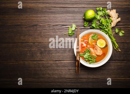 Soupe thaïlandaise traditionnelle épicée et chaude tom yum avec crevettes, citron vert, coriandre dans un bol sur fond de bois rustique avec espace pour le texte, vue du dessus. Banque D'Images