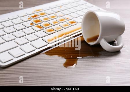 Tasse de café renversée sur le clavier de l'ordinateur sur une table en bois Banque D'Images