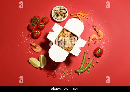 Composition à plat avec wok de nouilles et ingrédients sur fond rouge Banque D'Images