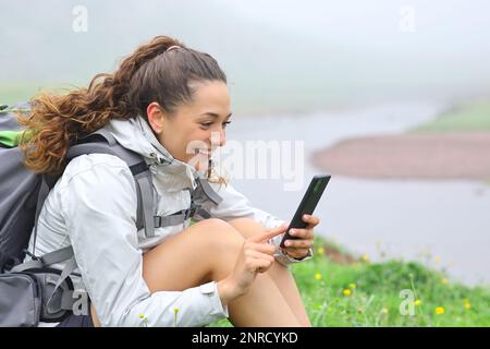 Joyeux randonneur utilisant un smartphone assis dans la nature au bord de la rivière Banque D'Images