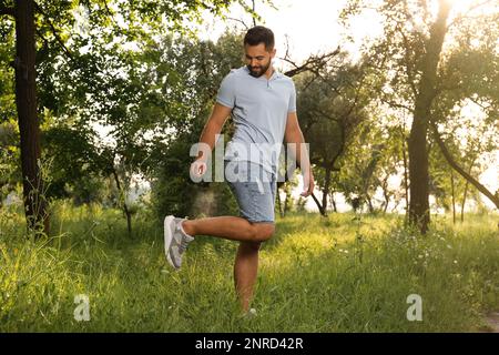 Homme appliquant un insectifuge sur la jambe dans le parc. Prévention des piqûres de tiques Banque D'Images