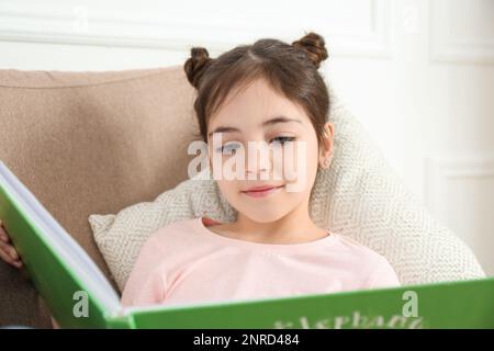 Petite fille lisant le livre dans un fauteuil à la maison Banque D'Images