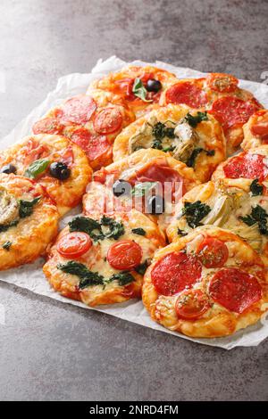 Mini-pizzas maison Pizzette avec des garnitures de viande et végétarienne gros plan sur le parchemin sur la table. Verticale Banque D'Images