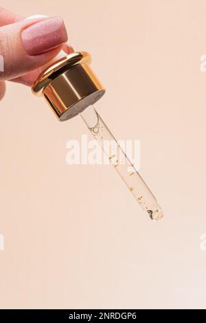 Main femelle avec Dropper d'huile essentielle, essence d'aromathérapie, sérum de beauté avec 24K d'or ou liquide médicinal sur fond beige. Flacons sans marque Banque D'Images