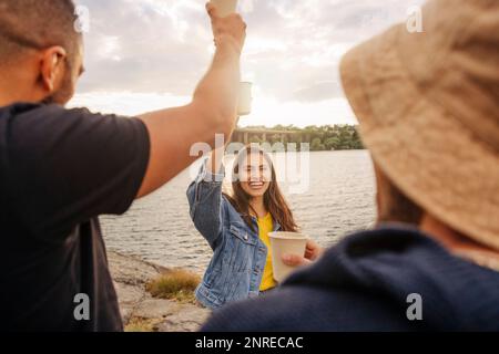 Bonne femme portant une veste en denim pour griller des boissons avec des amis pendant le pique-nique Banque D'Images