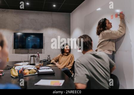 Une jeune femme d'affaires écrit sur des notes adhésives par des collègues hommes et femmes dans la salle de conseil Banque D'Images