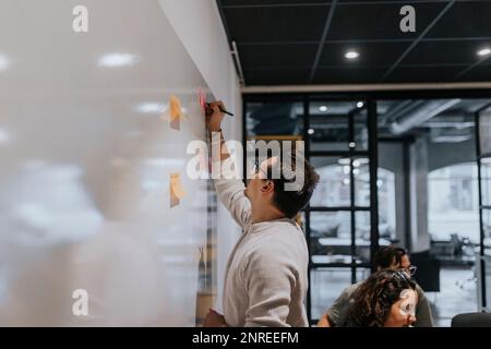 Un jeune homme entrepreneur écrit sur une note adhésive par des collègues du bureau de création Banque D'Images