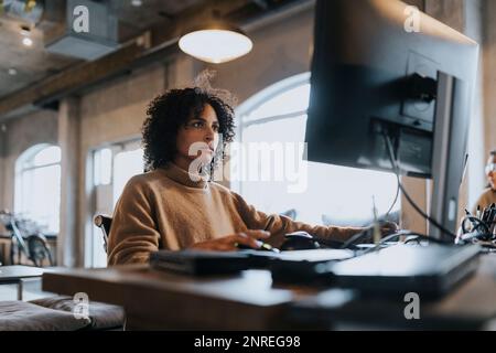 Hacker féminin dédié travaillant sur l'ordinateur au bureau dans la société de démarrage Banque D'Images