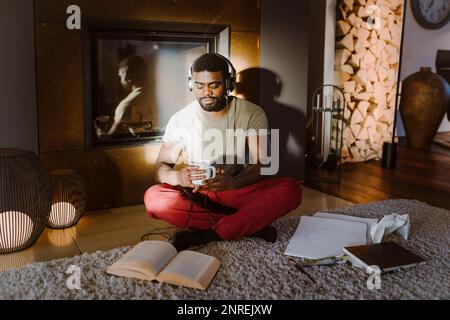 Un jeune homme écoute de la musique tout en lisant un livre à la maison Banque D'Images