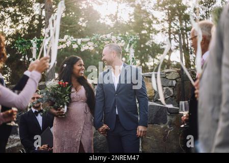 Couple joyeux et jeune tenant les mains tout en marchant parmi les invités lors de la cérémonie de mariage Banque D'Images