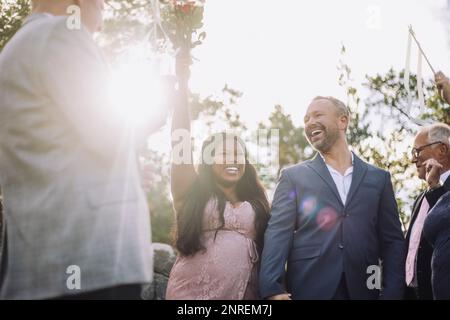 Jeune mariée tenant un bouquet d'honneur à la cérémonie de mariage avec marié parmi les invités Banque D'Images