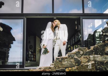Un couple adulte moyen affectueux s'embrassant à la bouche près du hall d'entrée pendant le jour du mariage Banque D'Images