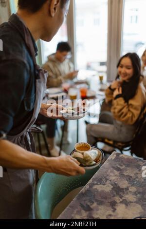 Serveur de sexe masculin servant des boulettes aux clients au restaurant Banque D'Images