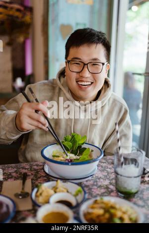 Portrait d'un jeune homme souriant avec des baguettes au restaurant Banque D'Images