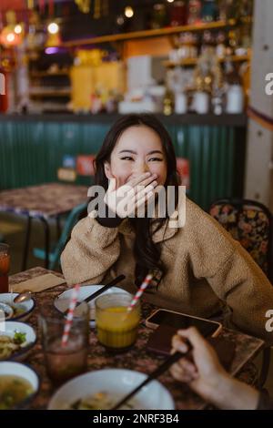 Une femme rit tout en couvrant la bouche au restaurant Banque D'Images