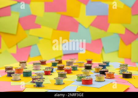 Bobines métalliques avec fil multicolore pour machine à coudre sur une table avec des notes adhésives en papier multicolore sur fond Banque D'Images