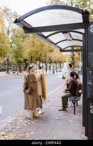 Des amis masculins et féminins parlent en attendant à l'arrêt de bus Banque D'Images