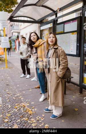 Des amies qui regardent loin en attendant à l'arrêt de bus Banque D'Images