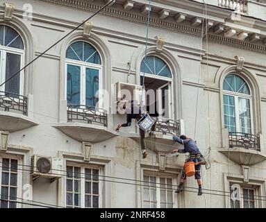 Bucarest, Roumanie - 21 février 2023. Alpiniste industriel en hauteur sur corde, mur de plâtrage avec truelle. Grimpeur industriel pour la réparation de la maison f Banque D'Images