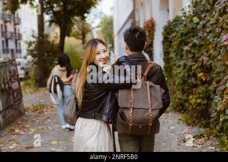 Vue arrière de l'homme marchant avec une amie qui regarde l'épaule sur le trottoir Banque D'Images