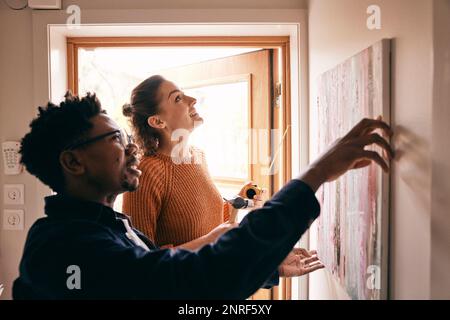 Couple s'aidant les uns les autres tout en accrochant la peinture sur le mur près de la porte à la maison Banque D'Images