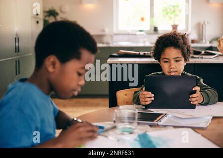 Garçon utilisant une tablette numérique tandis que frère colorant dans le livre à la maison Banque D'Images