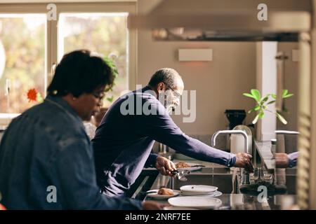 Homme senior qui allume le robinet tout en lavant les cuillères dans la cuisine à la maison Banque D'Images