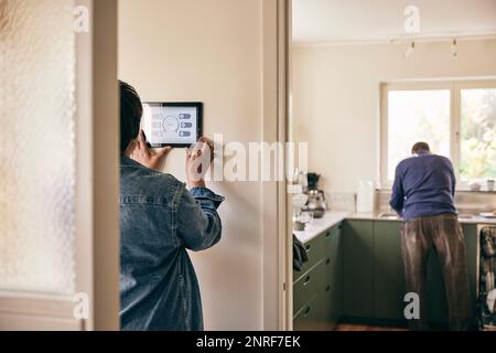 Vue arrière de la femme utilisant une tablette numérique montée au mur à la maison Banque D'Images