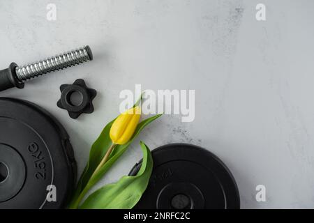 Gym haltères plaques de musculation, tulipes jaunes fleurs. Cadeau pour la fête des femmes, la fête des mères ou l'anniversaire. Séance d'entraînement de fitness avec espace de copie. Banque D'Images