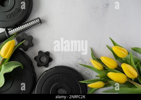 Gym haltères plaques de musculation, tulipes jaunes fleurs. Cadeau pour la fête des femmes, la fête des mères ou l'anniversaire. Séance d'entraînement de fitness avec espace de copie. Banque D'Images