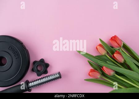 Gym dumbell barbell plaque de poids et tulipes fleurs en cadeau pour la Journée des femmes. Entraînement physique sain, entraînement sportif plat avec espace de copie. Banque D'Images