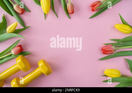 Des haltères de gym et des fleurs de tulipes en cadeau pour la fête des femmes ou l'anniversaire. Entraînement physique sain, entraînement sportif plat avec espace de copie. Banque D'Images