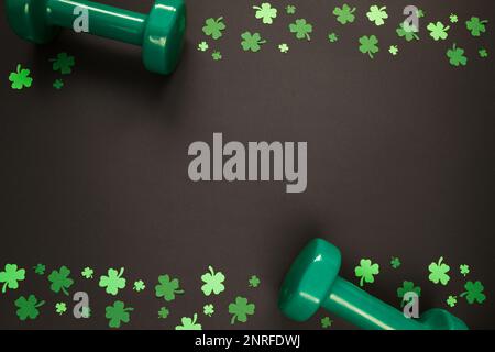 Deux haltères vertes et trèfle shamrock pour St. Patrick. Concept de composition de la mise en forme de la salle de gym. Copier l'espace sur fond noir. Banque D'Images